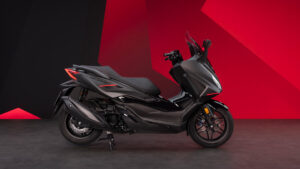 Scooter Honda Forza 350 noir, de profil, sur fond rouge et noir