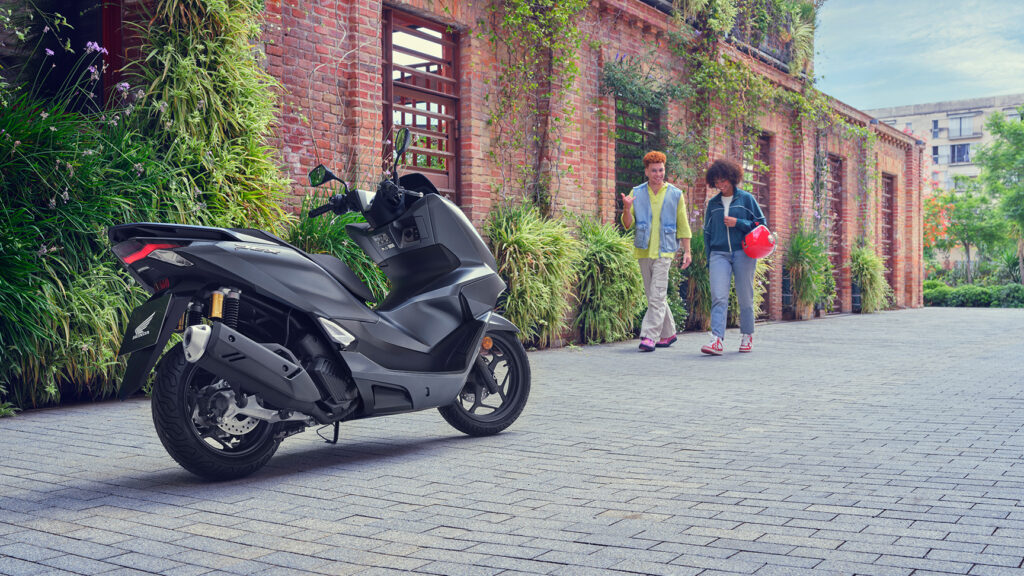 Scooter Honda PCX125 gris, de profil, dans une rue pavée