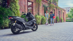 Scooter Honda PCX125 gris, de profil, dans une rue pavée