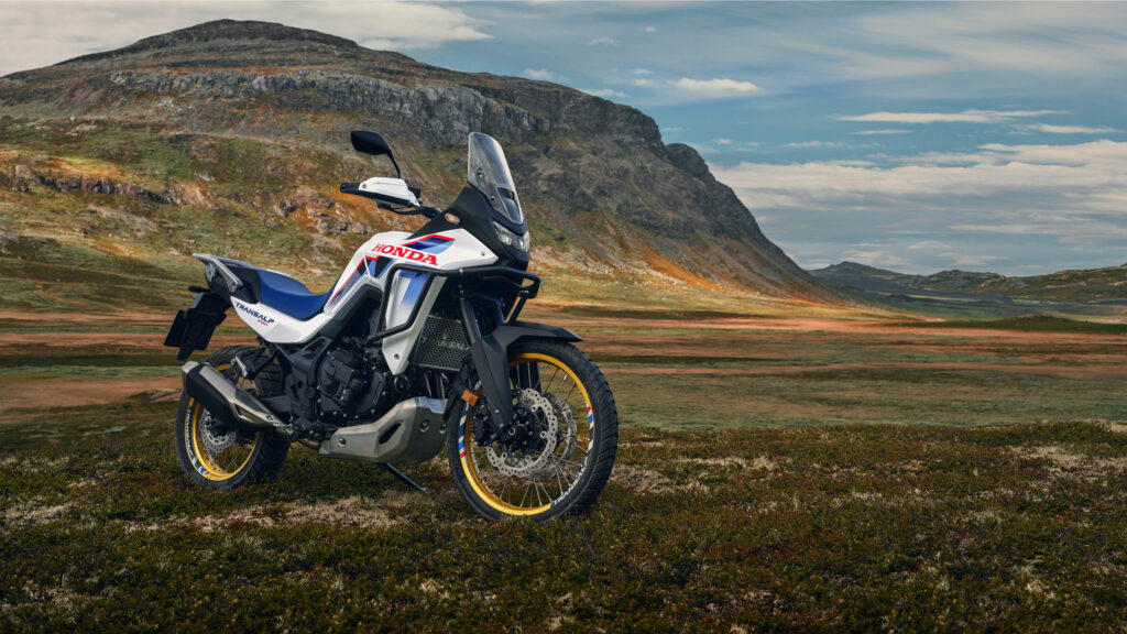 Honda XL750 Transalp en livrée tricolore, de profil, au bord d'un lac de montagne