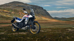 Honda XL750 Transalp en livrée tricolore, de profil, au bord d'un lac de montagne