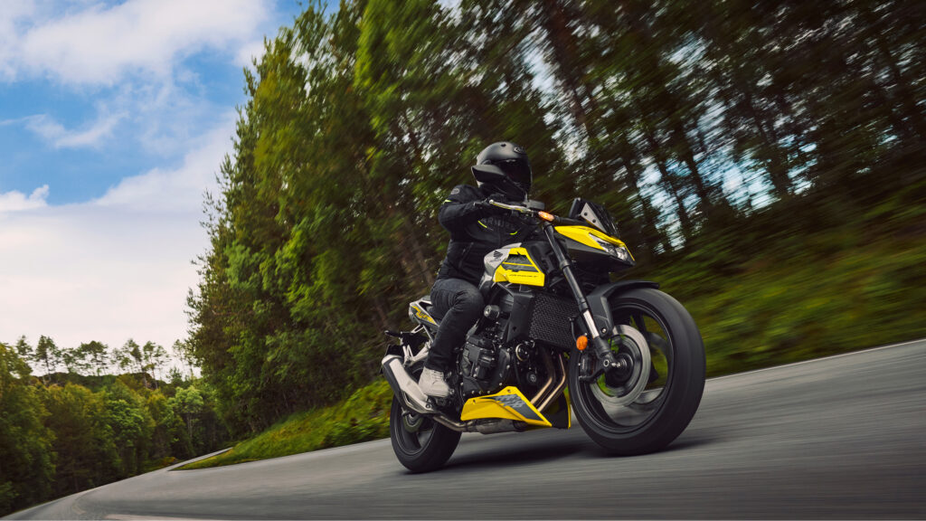Honda CB750 Hornet jaune sur une route de montagne bordée de sapins