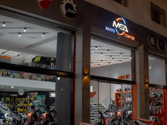 Façade éclairée du magasin MSA Moto Center à la nuit tombée, enseigne lumineuse et vitrines montrant motos et équipement pilote