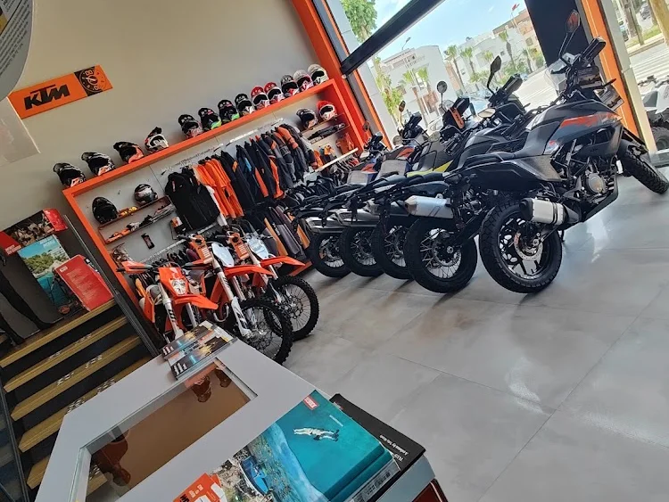 Rangée de motos trail et adventure alignées face à la baie vitrée, avec un mur de casques et de vestes sur la gauche