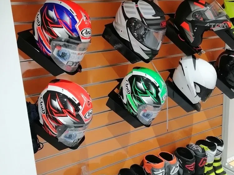 Mur de casques routiers sur panneau orange, avec une rangée de bottes de cross alignées au sol