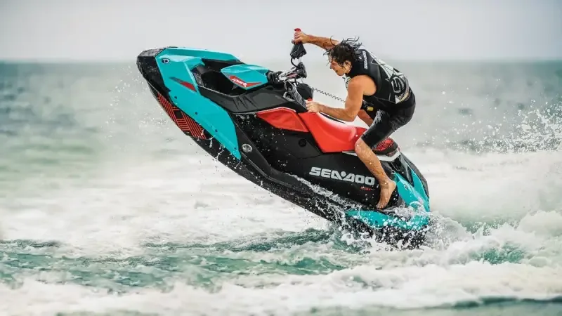 Un pilote debout sur un jet-ski Sea-Doo soulevé hors de l’eau, gerbe d’écume