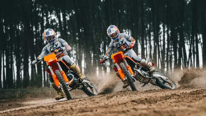 Deux pilotes de motocross en virage sur une piste de terre bordée de pins