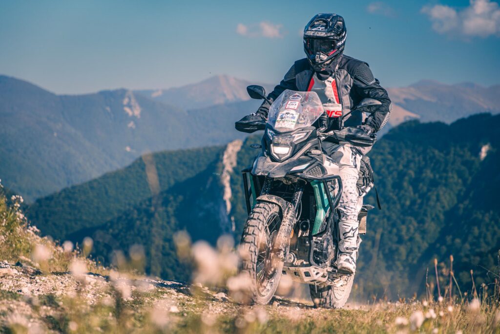 KOVE 510X verte et grise, pilote casqué roulant de face sur un sentier de crête en montagne