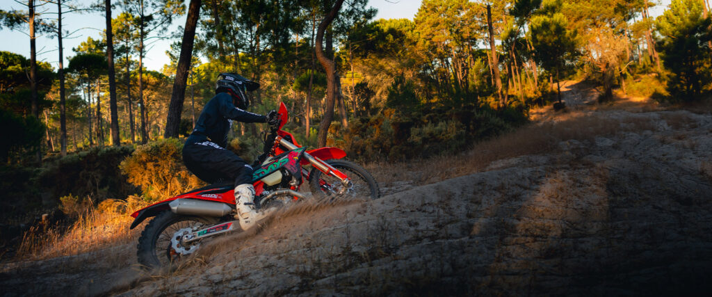 KTM 250 EXC-F Six Days 2027 en montée sur une piste sableuse au soleil couchant