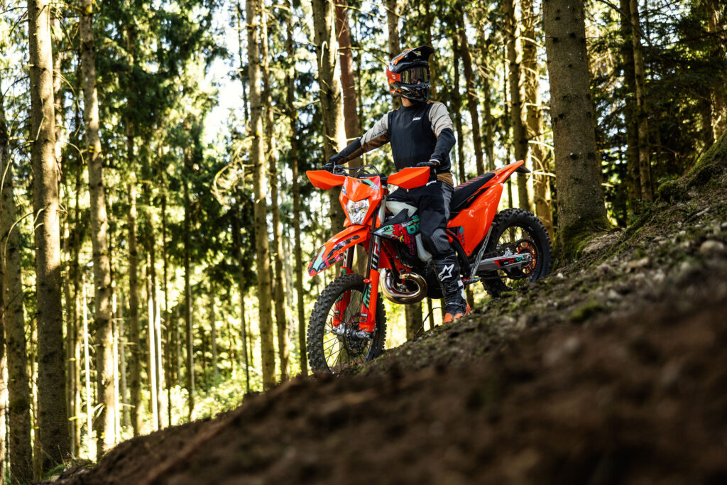 KTM 300 EXC Six Days 2027 à l'arrêt sur une pente en forêt, pilote en selle