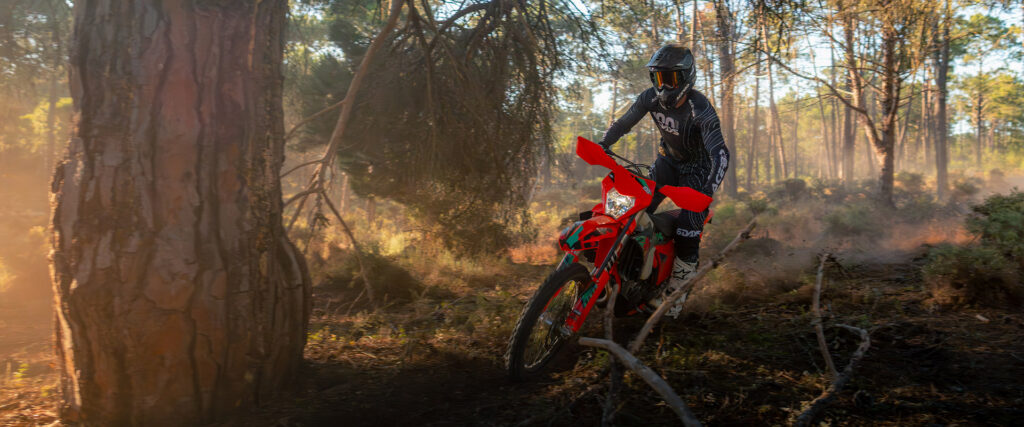 KTM 450 EXC-F Six Days 2027 dans un sous-bois de pins, phare allumé