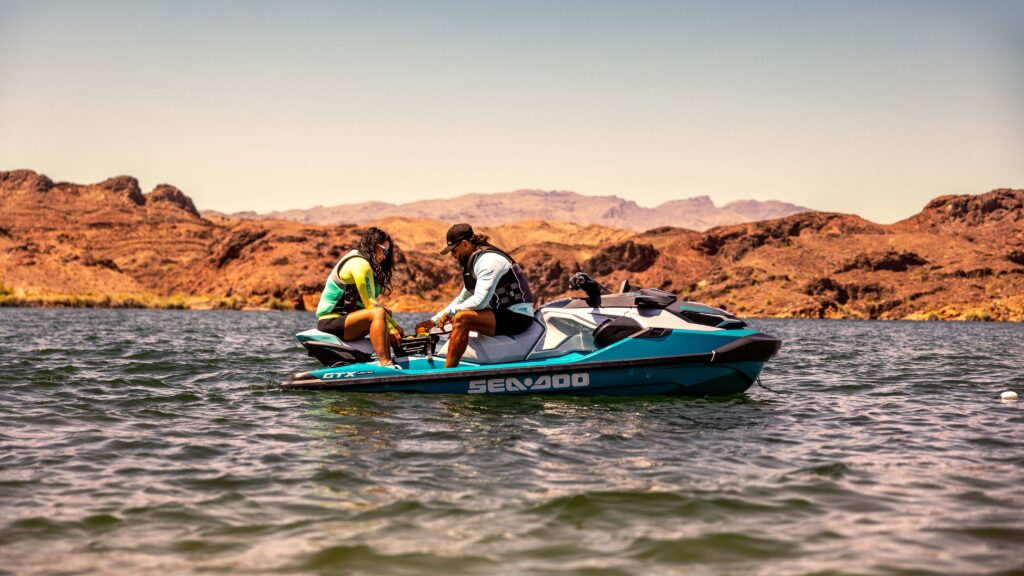 Deux passagers en Sea-Doo GTX Limited 325 bleu sarcelle sur un lac bordé de falaises rouges, vue lointaine