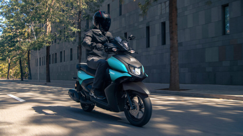 Pilote casqué sur un Yamaha Cygnus Ray ZR 125 cyan mat dans une rue ombragée
