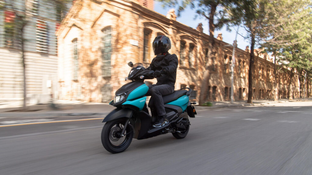 Yamaha Cygnus Ray ZR 125 cyan mat en circulation le long d'un mur de brique