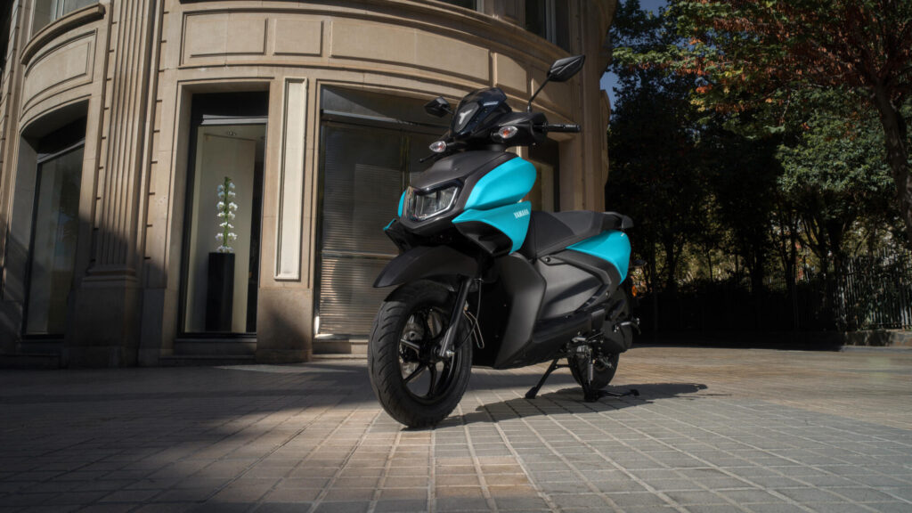 Yamaha Cygnus Ray ZR 125 cyan mat stationné devant l'entrée d'un immeuble ancien