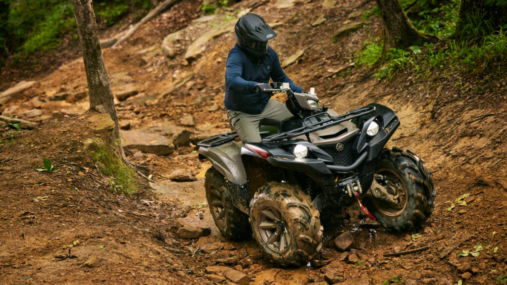 Pilote casqué sur un Yamaha Grizzly 700 EPS XT-R franchissant des rochers en forêt