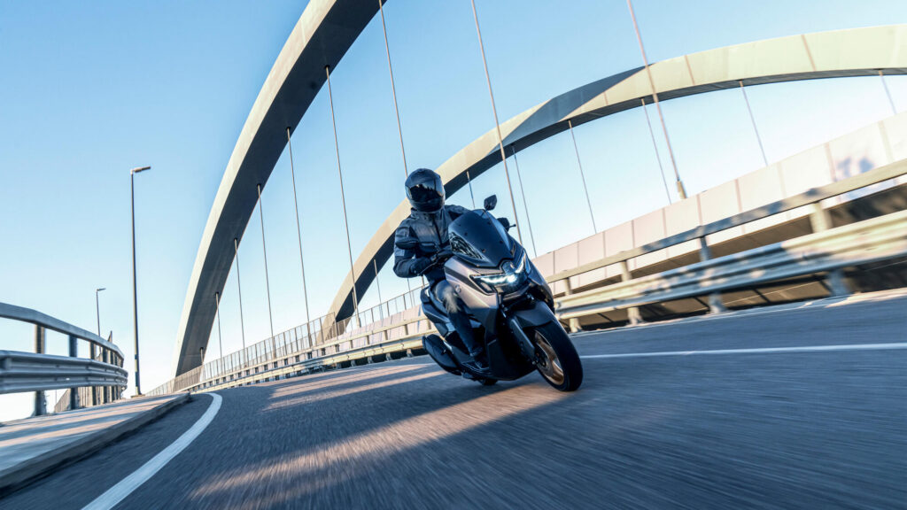 Yamaha NMAX Tech Max gris anthracite à jantes bronze en courbe sous un pont en arc