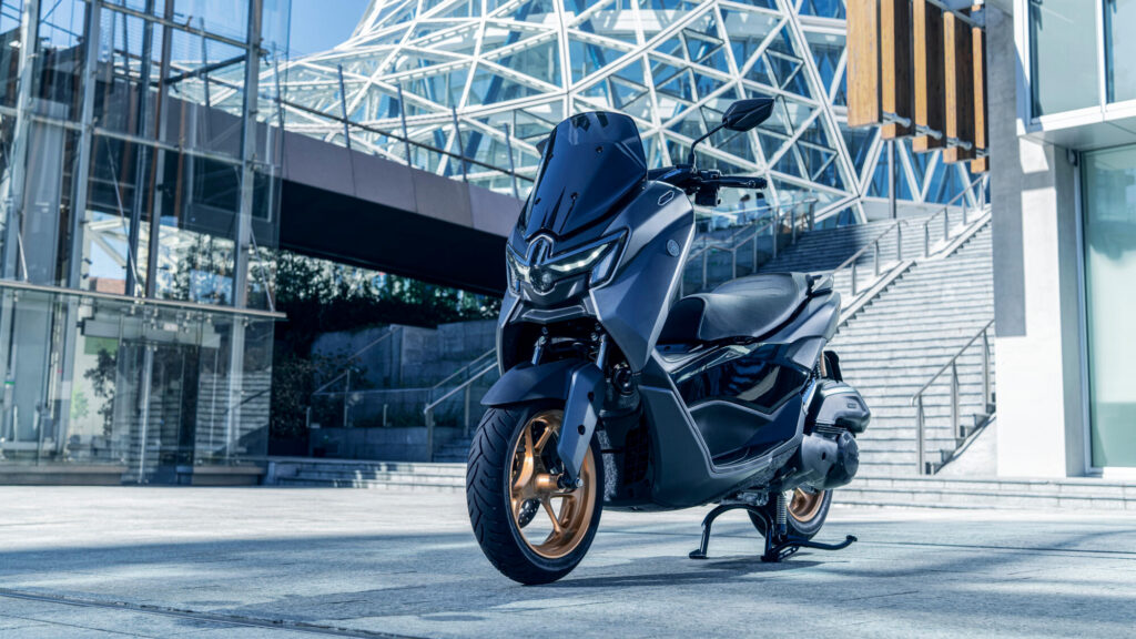 Yamaha NMAX Tech Max gris anthracite à jantes bronze stationné au pied d'un escalier, devant une façade vitrée