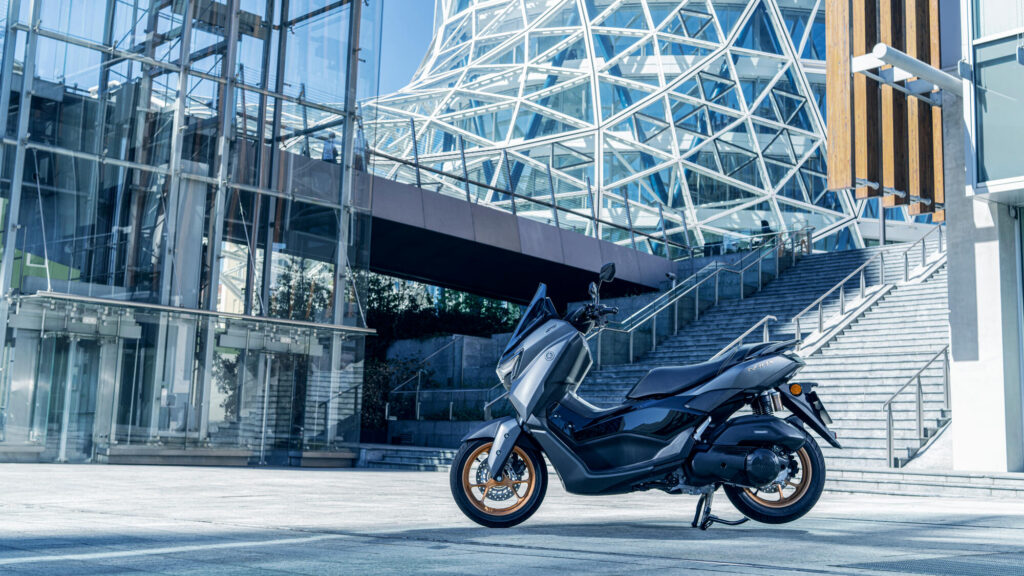 Yamaha NMAX Tech Max gris anthracite à jantes bronze stationné devant un immeuble vitré