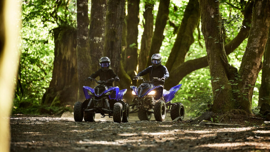 Deux quads Yamaha Raptor 110 bleus avançant dans une forêt