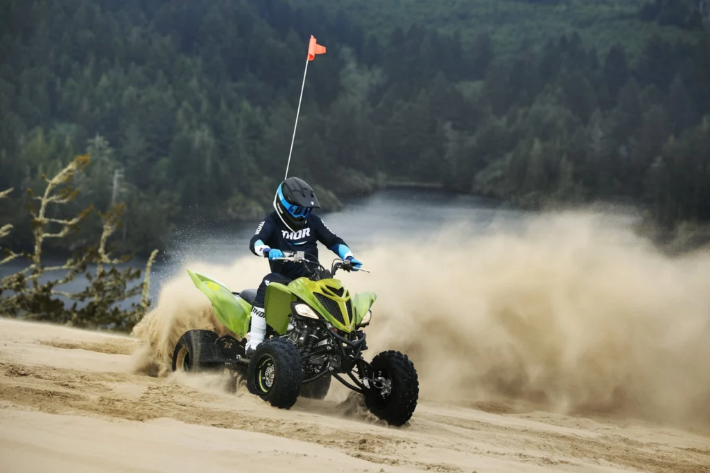 Pilote casqué en glisse sur un Yamaha Raptor 700R SE vert dans les dunes, au bord d'un lac
