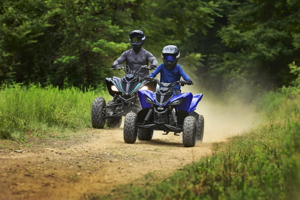 Deux jeunes pilotes casqués sur des quads Yamaha Raptor 90 sur un chemin de terre