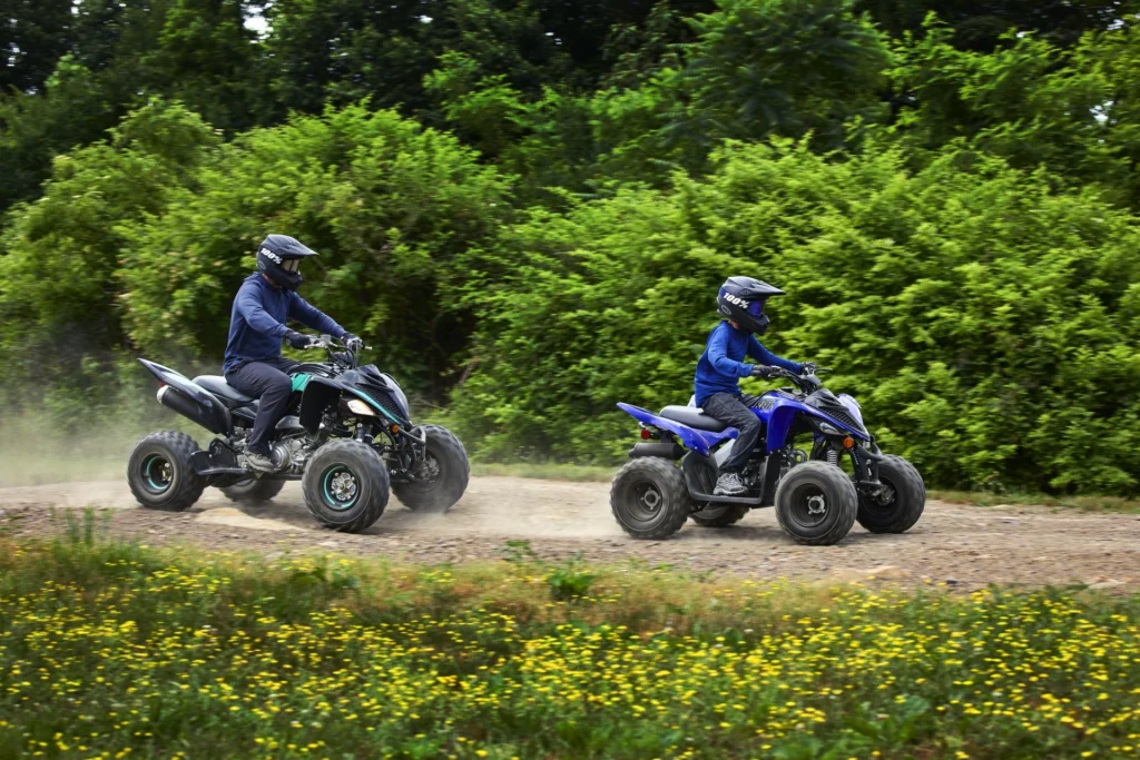 Deux quads Yamaha Raptor 90 roulant sur une piste en lisière de forêt