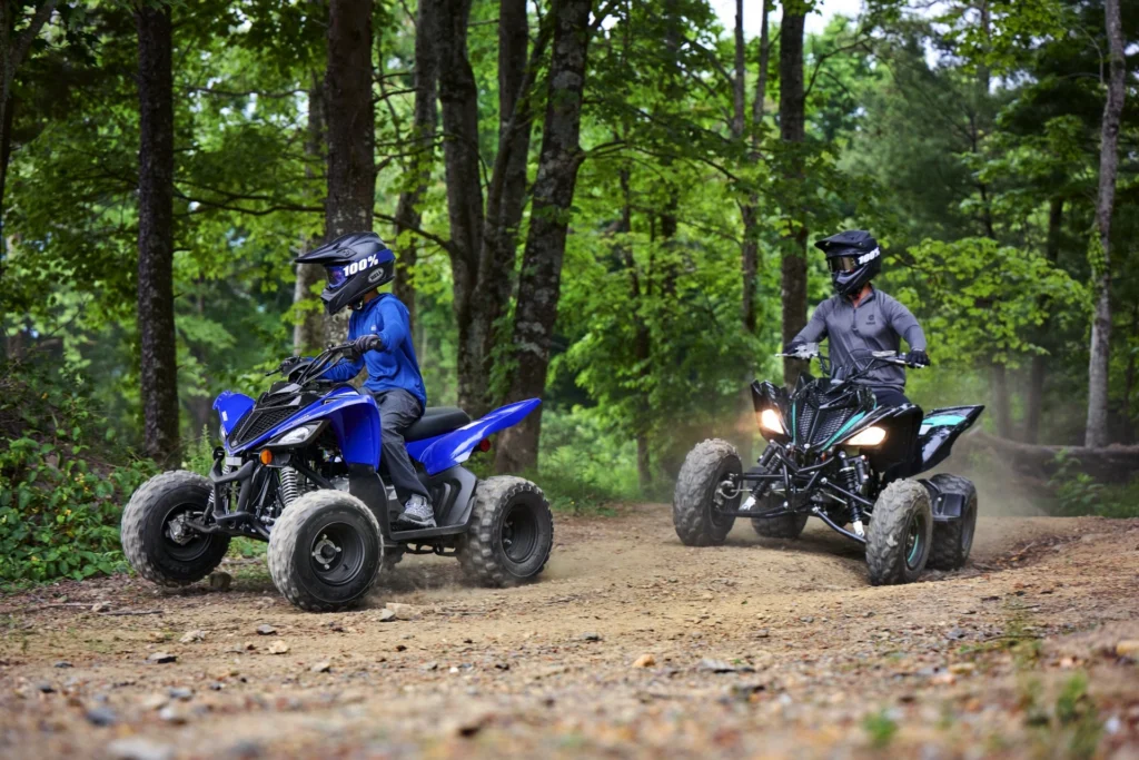 Jeunes pilotes casqués sur des Yamaha Raptor 90 bleus dans un sous-bois