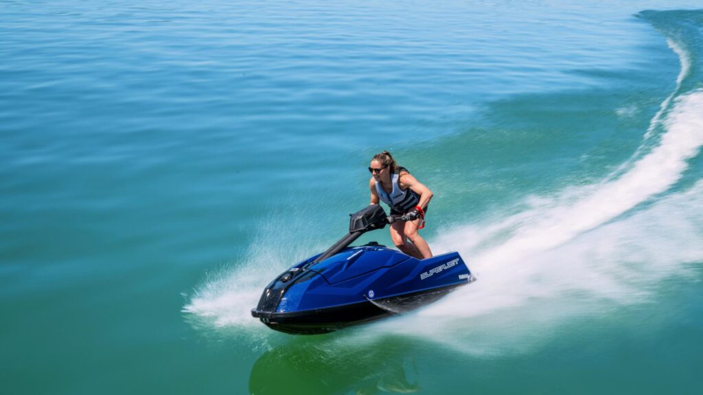 Pilote debout sur un Yamaha SuperJet bleu nuit en virage, laissant un sillage d'écume sur une eau turquoise